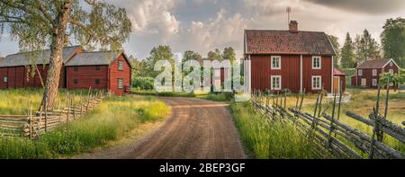 Piccola strada di campagna e vecchi cottage tradizionali rossi in un paesaggio rurale presso il villaggio Stensjo by. Oskarshamn, Smaland, Svezia, Scandinavia Foto Stock