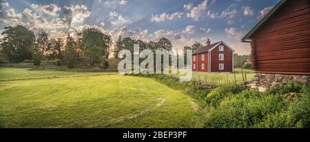 Piccola strada di campagna e vecchi cottage tradizionali rossi in un paesaggio rurale presso il villaggio Stensjo by. Oskarshamn, Smaland, Svezia, Scandinavia Foto Stock