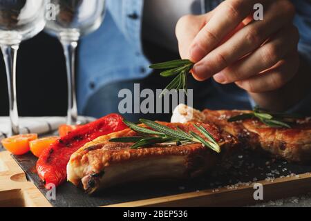 Persona mette il rosmarino sulla bistecca. Composizione con cibo alla griglia Foto Stock