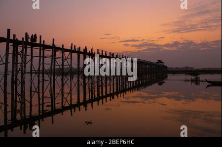 Sunrise U Bein-bridge con alcune persone irriconoscibili a piedi sulla più lunga passerella in legno di teak del mondo, Mandalay, Myanmar Foto Stock