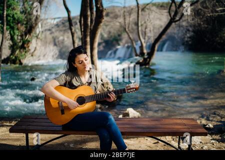 Giovane chitarrista che suona la chitarra acustica e che guarda alla natura fluviale.Ricerca di ispirazione.Creatore musicale.nuovo artista di buon umore.talento musicale.sorridente Foto Stock