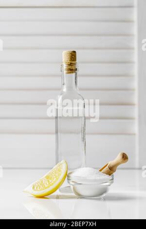Acido citrico in una piccola ciotola di vetro, aceto bianco in una bottiglia e una fetta di limone su fondo brillante, ingredienti del detergente fai da te Foto Stock
