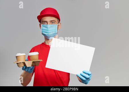 Corriere in uniforme rossa, maschera protettiva e guanti per la consegna di cibi e caffè da asporto. Servizio di consegna in quarantena. Tenendo un segno bianco per il testo Foto Stock