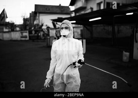 Addetto all'assistenza sanitaria che spruzza disinfettante con pistola a spruzzo in tuta per nocciole, maschera N95 e attrezzatura di protezione.dispositivi di protezione privati (DPI).Quaran Foto Stock