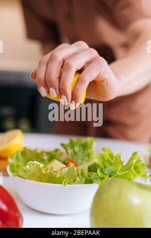 Primo piano delle mani delle donne che spremono il succo dal limone nel recipiente per insalate. Foto Stock