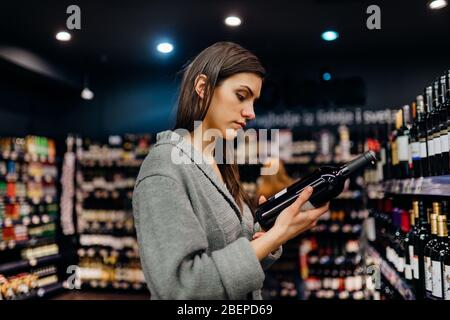 Donna che acquista per vino costoso in supermercato alcol store.choosing e l'acquisto buon vino a buon mercato.benefici di bere wine.Resveratrol.Everyday bing Foto Stock