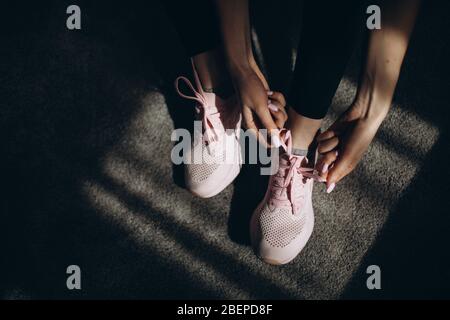 Primo piano delle sneaker sportive femminili con allacciatura a mani su tappeto. La ragazza di idoneità sta andando esercitarsi nel paese. Attenzione selettiva sulle scarpe in atmosfera oscura. Foto Stock