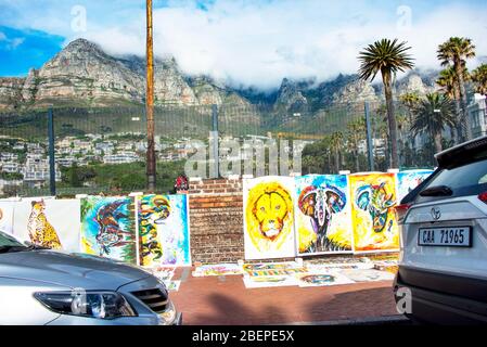 Poster di arte africana fiancheggiano il muro in una strada fuori di Città del Capo. La catena montuosa dei dodici Apostoli è sullo sfondo. Le immagini sono moderne e di fauna selvatica. Foto Stock