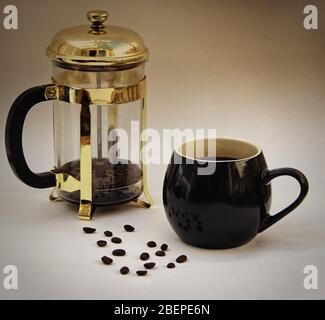 Il concetto di una casalinga caffè del mattino, con una tazza di caffè nero, ambientato contro un cafetiere e un modello casuale di chicchi di caffè Foto Stock