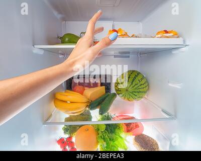 Donna a mano a prendere qualcosa da un frigo aperto. Vista in prima persona Foto Stock