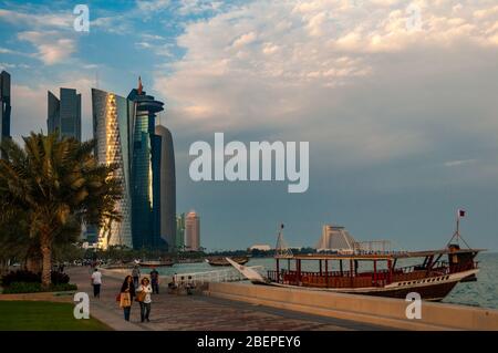 La gente a piedi passato un dhow su Al Corniche con la torre di Doha e moderni edifici di West Bay in background. Foto Stock
