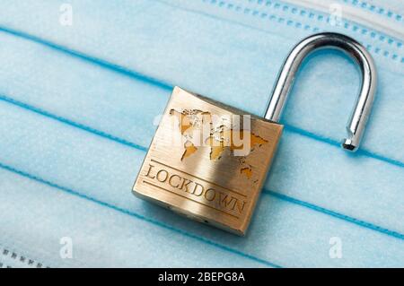 Fine del lockdown mondiale del coronavirus: Un lucchetto aperto con una mappa del mondo e la parola lockdown incisa su una maschera chirurgica blu chiaro. Foto Stock