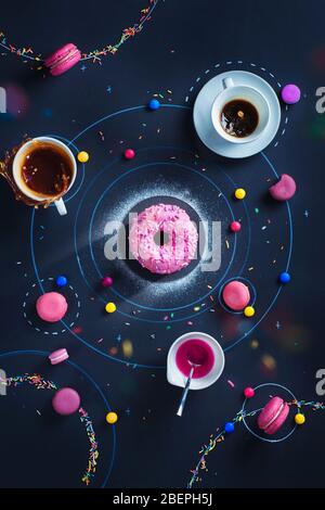 Piatto creativo con ciambella spaziale, stelle di macaron e orbite, spruzzi cadenti e splash di tè Foto Stock