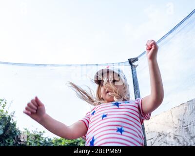 Una ragazza di quattro anni salta su un trampolino nel suo giardino urbano a Londra, Regno Unito Foto Stock