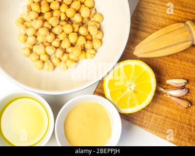 Ciotole di olio di oliva di ceci e tahini con spicchi d'aglio mezzo limone e spremiagrumi per fare l'hummus Foto Stock