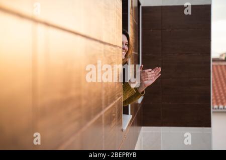 Giovane donna in quarantena applaudendo per sostenere gli operatori sanitari Foto Stock