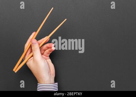Immagine creativa delle bacchette di legno nelle mani di sesso maschile su sfondo nero. Il giapponese e il cinese del cibo con copia spazio. Foto Stock