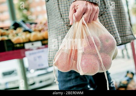 la prima parte di un uomo, lo shopping ad un greengrocer o ad un mercato di strada, con alcuni sacchetti di maglia riutilizzabili tessili pieni di frutta e verdura, come misura al rosso Foto Stock