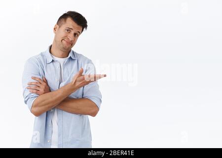 Ritratto di scettico bel giovane uomo smirk incerto, introdurre qualcosa, presentare o mostrare il prodotto con qualità sospetta, puntando a destra Foto Stock