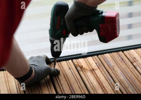 Fai da te costruzione di un portico / balcone pavimento con tavole di legno marrone a Espoo, Finlandia, febbraio, 2020. Persona che usa la macchina di perforazione per costruire il pavimento. Foto Stock