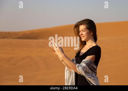 giovane donna fotografa un tramonto nel deserto sul suo smartphone. Foto Stock