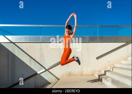 donna che indossa abbigliamento sportivo arancione che salta in aria, Foto Stock