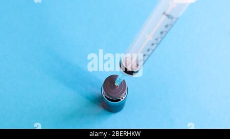 Una siringa fuoriesce da un flacone di liquido rosso. Isolato su uno sfondo blu. Medicina, iniezioni, vaccini e siringhe monouso, concetto di farmaco. STER Foto Stock