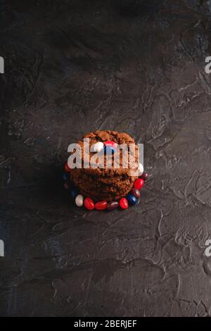 Biscotti fatti in casa al cioccolato con cereali con succosi fagioli di gelatina su sfondo nero scuro testurizzato, vista angolare Foto Stock