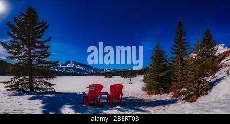 Sedie rosse sotto un cielo invernale illuminato dalla luna al Two Jack Lake, Banff National Park, Canada. Foto Stock