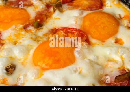 Uova fritte con pomodori in un primo piano in padella come sfondo Foto Stock