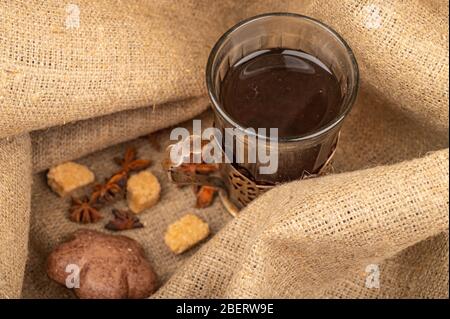 Un bicchiere sfaccettato di tè in un portabicchieri vintage, bagel, biscotti e pan di zenzero al cioccolato su uno sfondo di tessuto grezzo casalingo. Primo piano Foto Stock