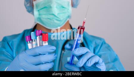 Il medico in blu indossa il respiratore e i guanti in lattice per tenere provette con analisi del sangue. Concetto di analisi del sangue per coronavirus Foto Stock