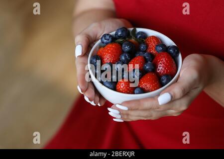 Ragazza in abito rosso che tiene piatto di bacche. Piatto bianco con fragola e mirtillo. Stile di vita sano. Vitamina di frutta. Macedonia di frutta Foto Stock