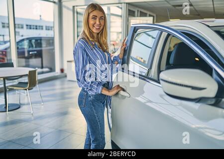 Ragazza felice che apre la porta dell'auto nello showroom dell'auto. Foto Stock