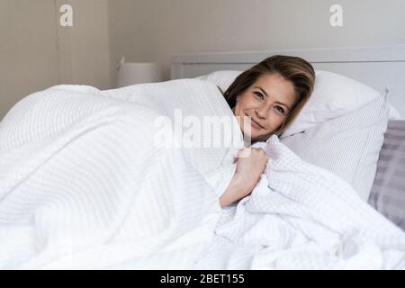 donna matura e carina che dorme sotto il piumone sul letto Foto Stock