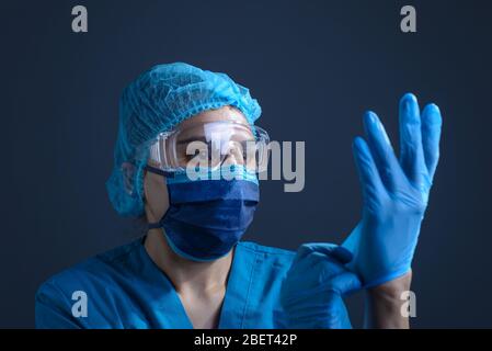 protezione contro l'infezione da coronavirus. Ritratto di una ragazza medico, infermiere, in un vestito protettivo, occhiali e una maschera, indossa guanti medici. Studio pho Foto Stock