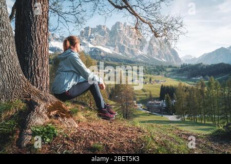 Giovane donna con occhiali da sole e giacca blu è seduta sulla collina Foto Stock