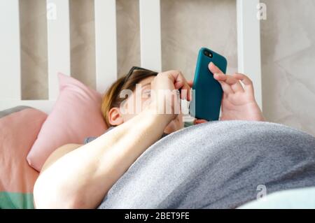 la ragazza incinta si trova sul letto e guarda il telefono Foto Stock