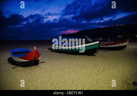 Portogallo, sera spiaggia di Nazare, barche di legno colorate, vista panoramica del faro di Nazare, tradizionali barche da pesca portoghesi a Nazare sulla costa Foto Stock