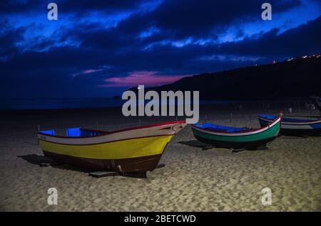 Portogallo, sera Nazare spiaggia nel mese di giugno, barche in legno colorato, vista panoramica del faro Nazare, tradizionali barche da pesca portoghese a Nazare su t. Foto Stock