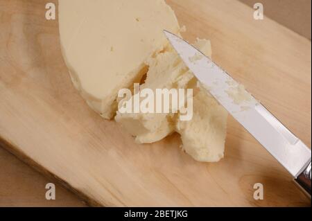 Pezzo di formaggio cremoso di burro fatto in casa da spalmare. Tagliare a pezzi con un coltello su un asse di legno. Ottimo per colazione, delizioso cibo salato al mattino. Foto Stock