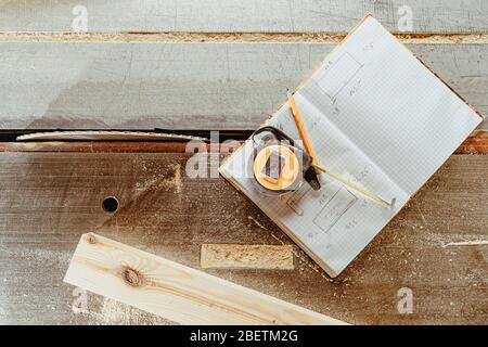 strumenti per la progettazione di un prodotto in legno: metro, matita e libro di lavoro su banco in una falegnameria Foto Stock