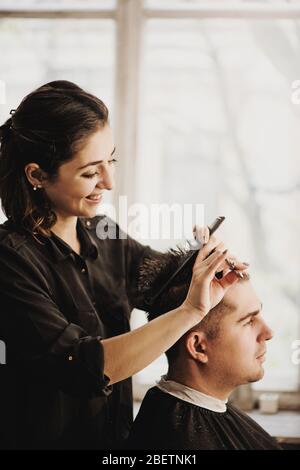 Vista ravvicinata del parrucchiere che taglia i capelli dell'uomo nel salone. Foto Stock