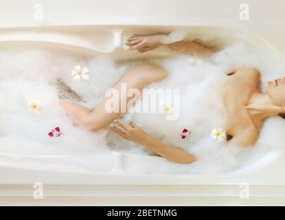 Vista dall'alto della bellissima donna che si rilassa in bagno con schiuma e fiori. Foto Stock