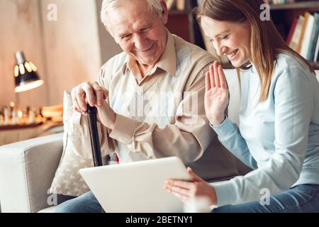 Padre e figlia a casa libreria seduta a guardare video chiamata sul laptop sventolando felice Foto Stock