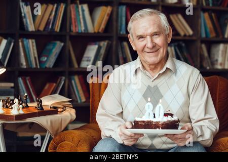 Uomo anziano da solo seduto alla biblioteca tenendo torta sorridente felice Foto Stock