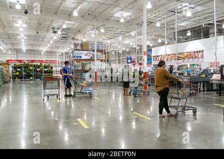 Kennesaw, GA / USA - 04/05/20: Persone mascherate in attesa in linea al checkout esercitandosi a distanza sociale in piedi 6 piedi di distanza via linee a terra a Cos Foto Stock