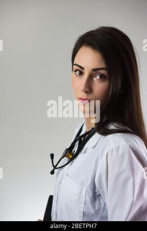 Stetoscopio femminile per uso medico intorno al collo isolato su sfondo grigio. Giovane femmina attraente con bel sorriso. Foto Stock