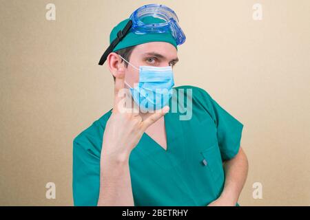 Medico in tuta protettiva verde e guanti sentirsi felice, facendo rock o pesante segno di metallo con la mano. Foto Stock
