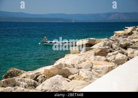 Barca da pesca vicino alla costa di pietra passeggiata di Brac di fronte a Hvar isola, mare Adriatico, Croazia Foto Stock